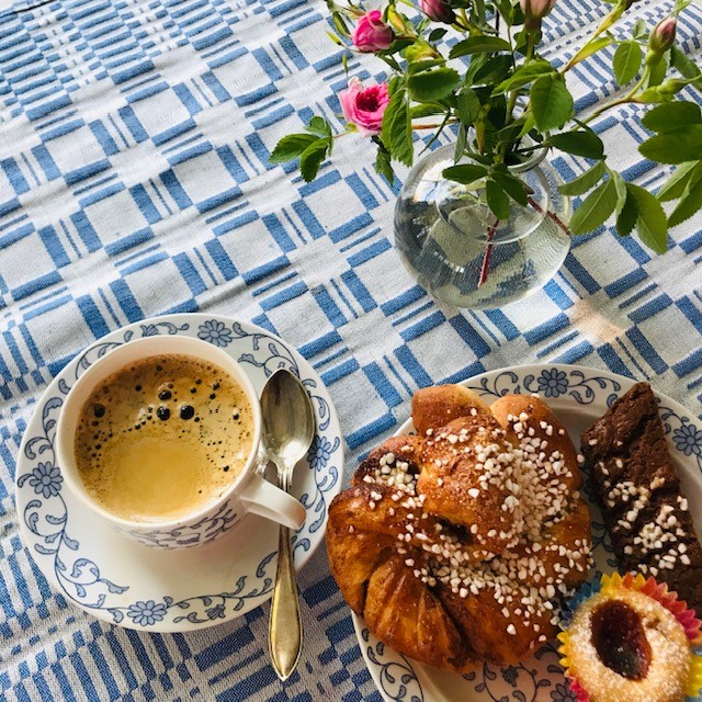 Blue & white checkered tablecloth with a cinnamon bun, cup of coffee, and flowers